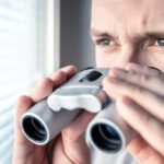 Man looking out window with binoculars