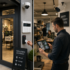 Security camera, keypad, card reader at business entrance; man views security footage on tablet inside.